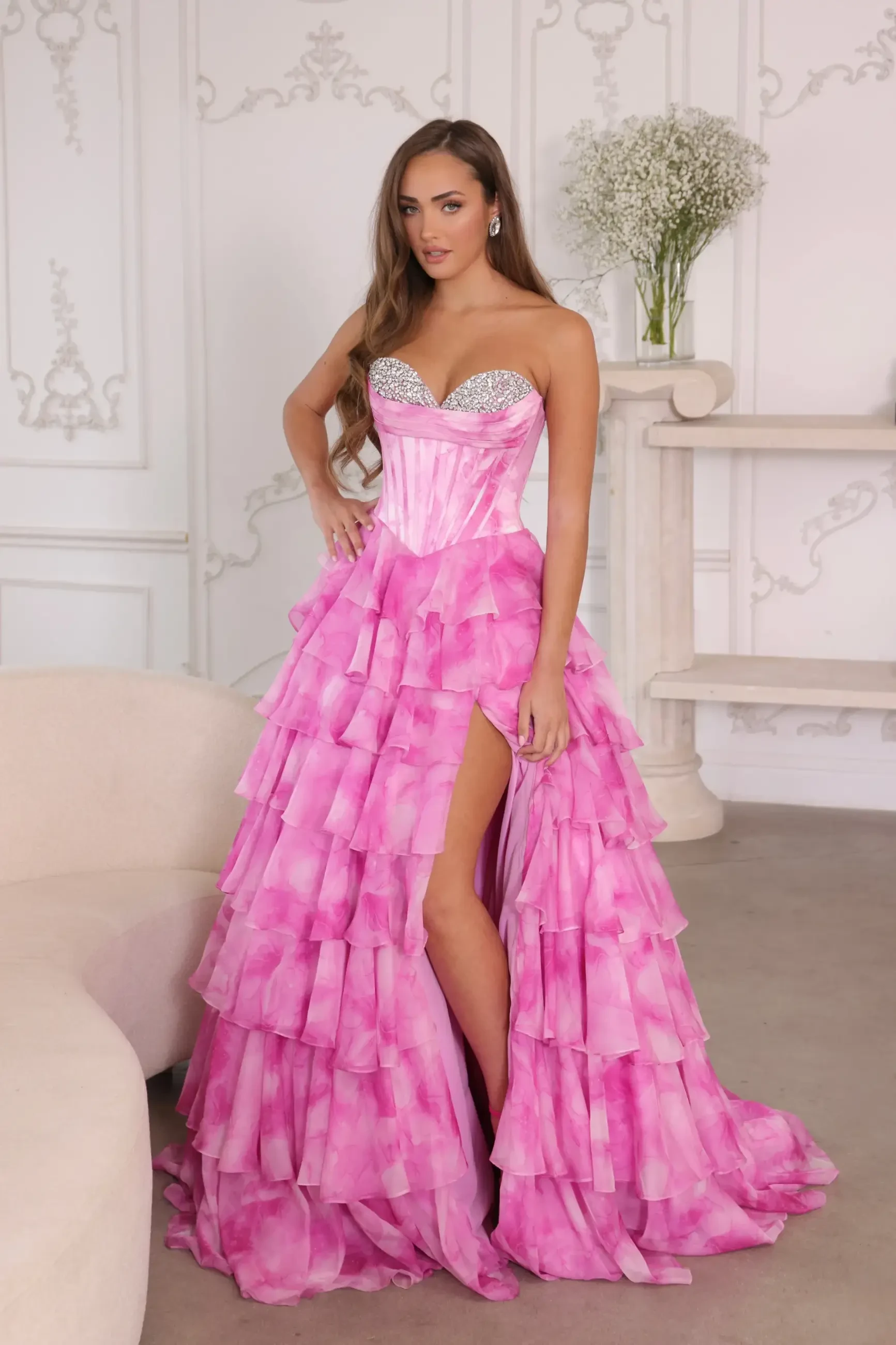 Model is wearing a strapless ball gown with a corset bodice and a voluminous tiered ruffle skirt