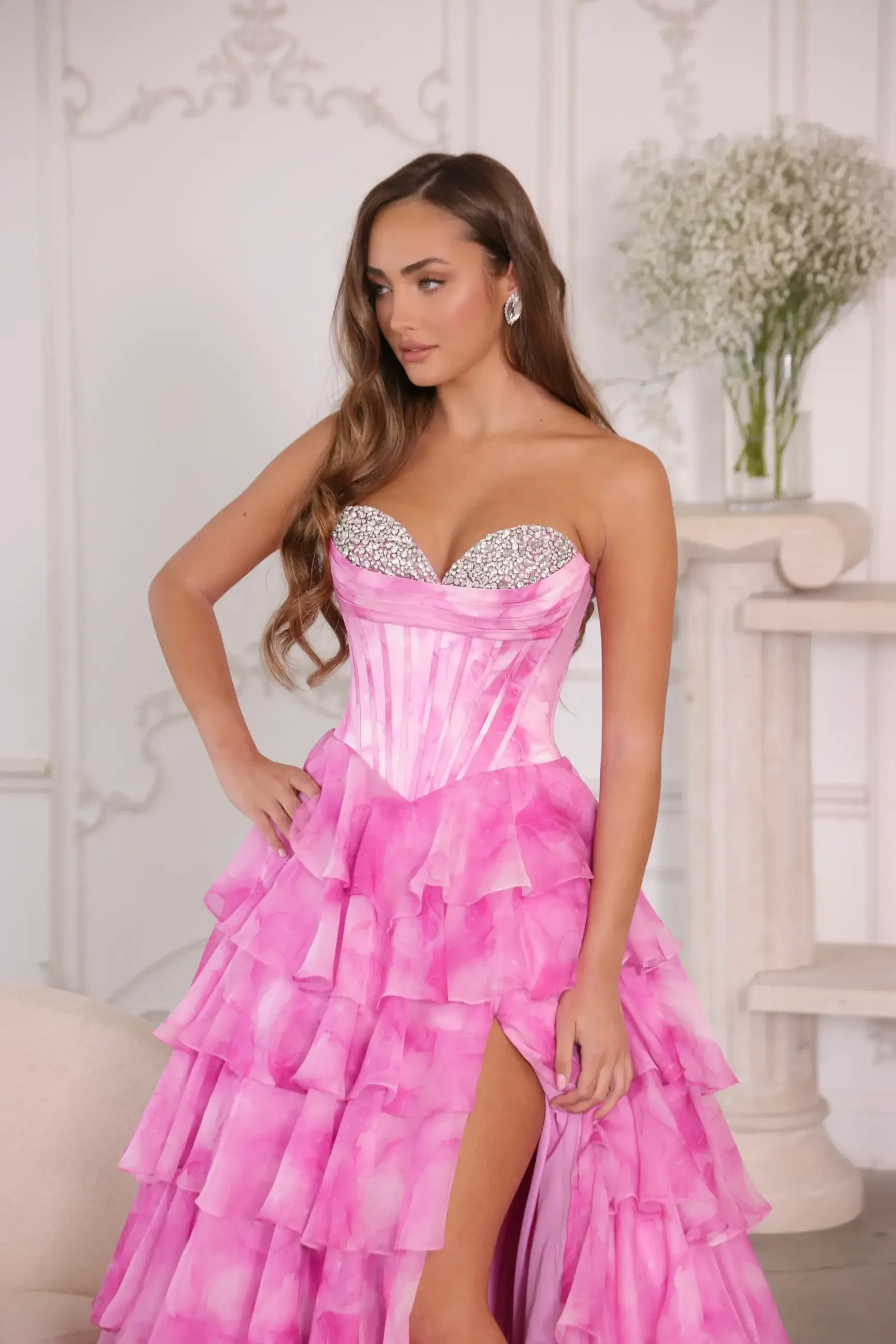 Model is wearing a strapless ball gown with a corset bodice and a voluminous tiered ruffle skirt
