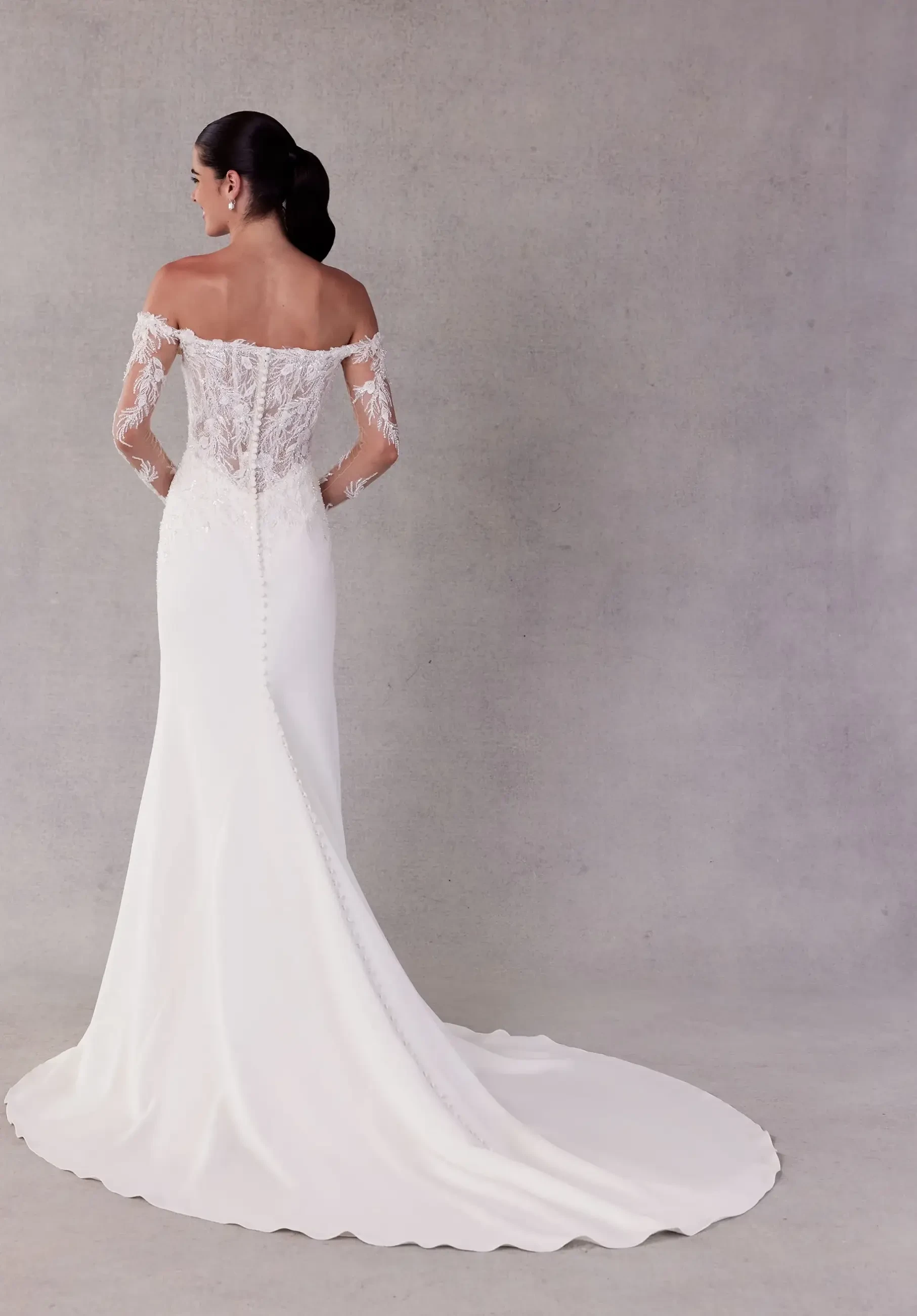 Model is wearing an off the shoulder long sleeve basque waist wedding dress by morilee