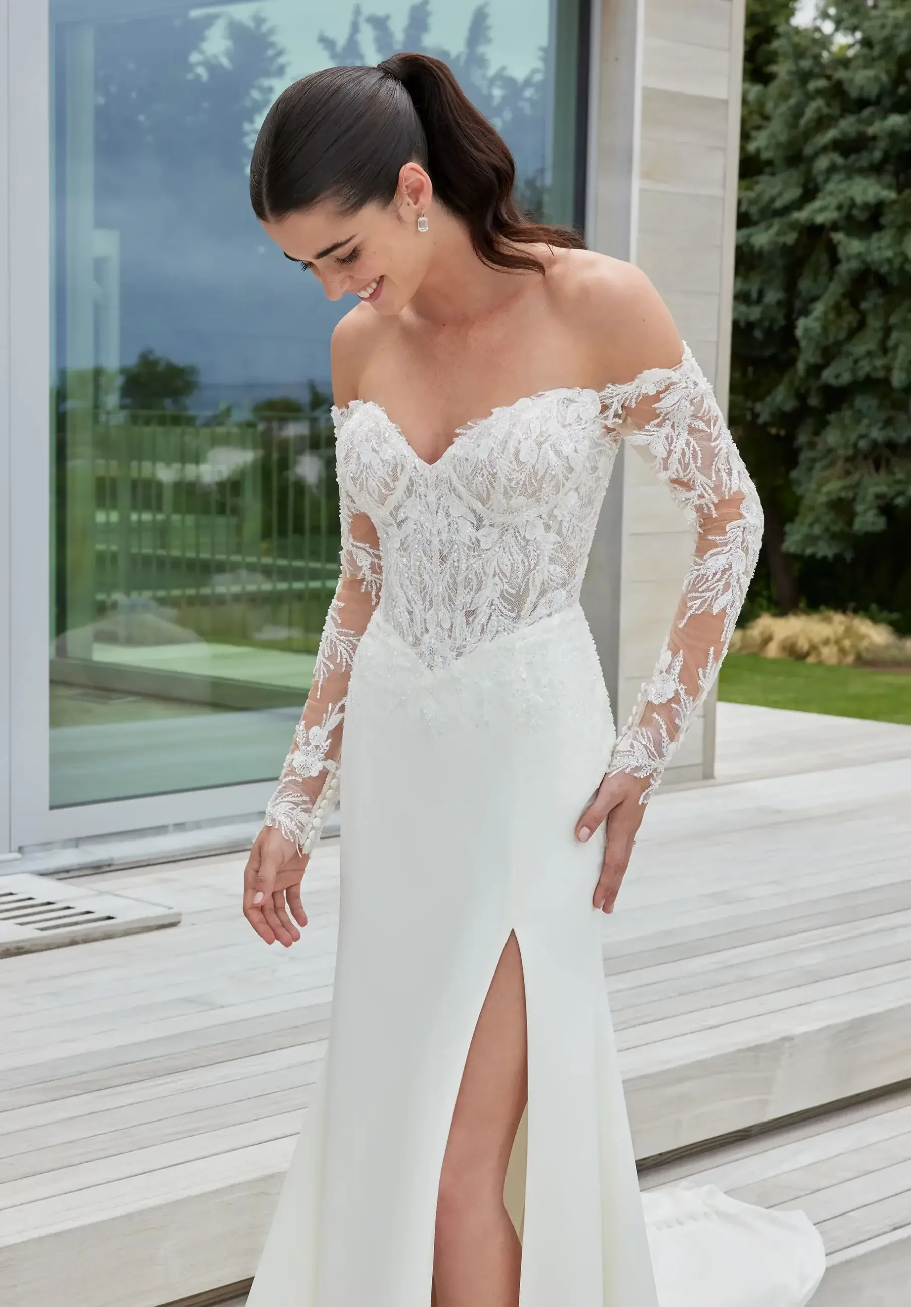 Model is wearing an off the shoulder long sleeve basque waist wedding dress by morilee