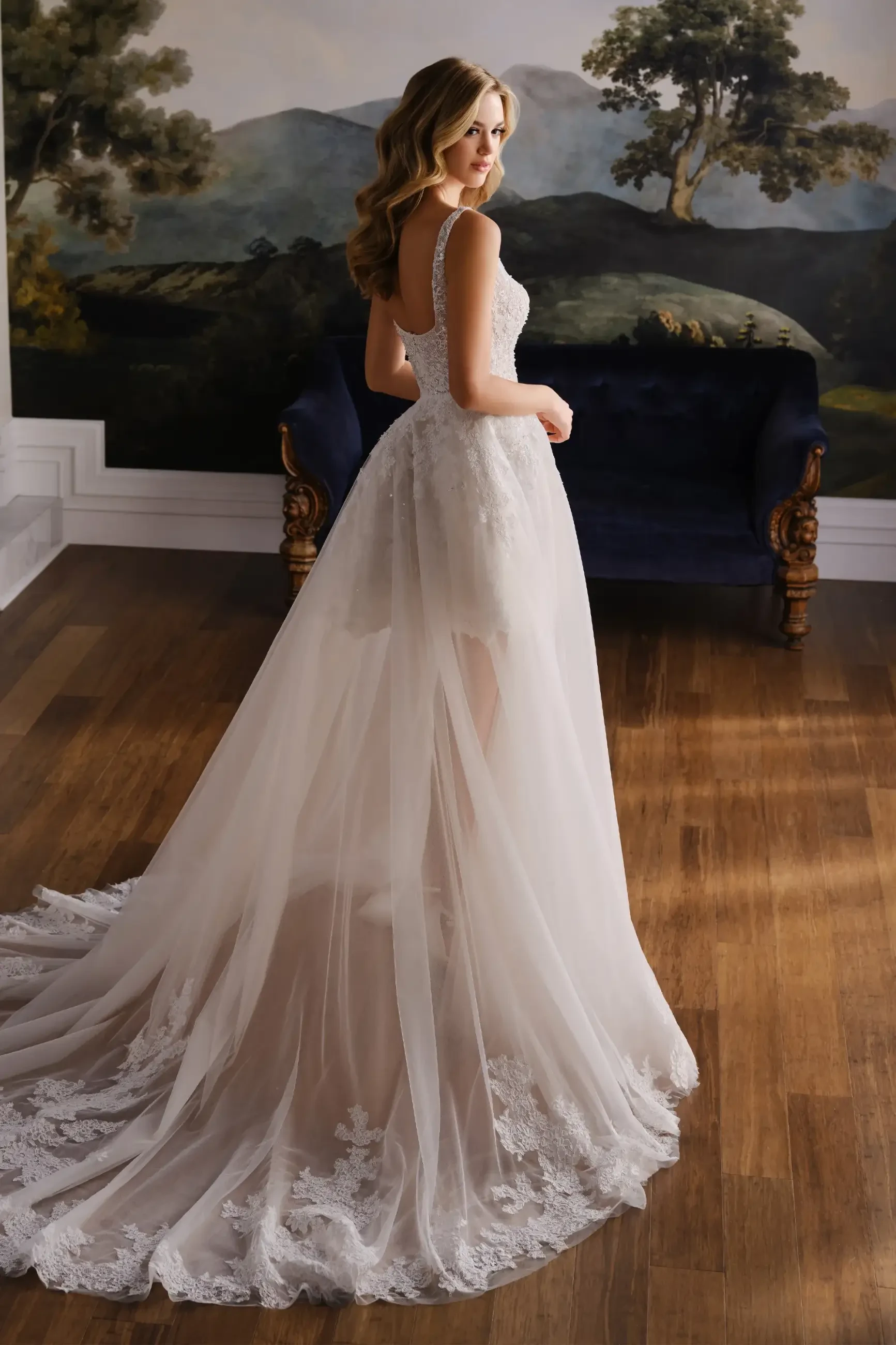 Model is wearing a lace mini wedding dress with a square neckline and a detachable overskirt