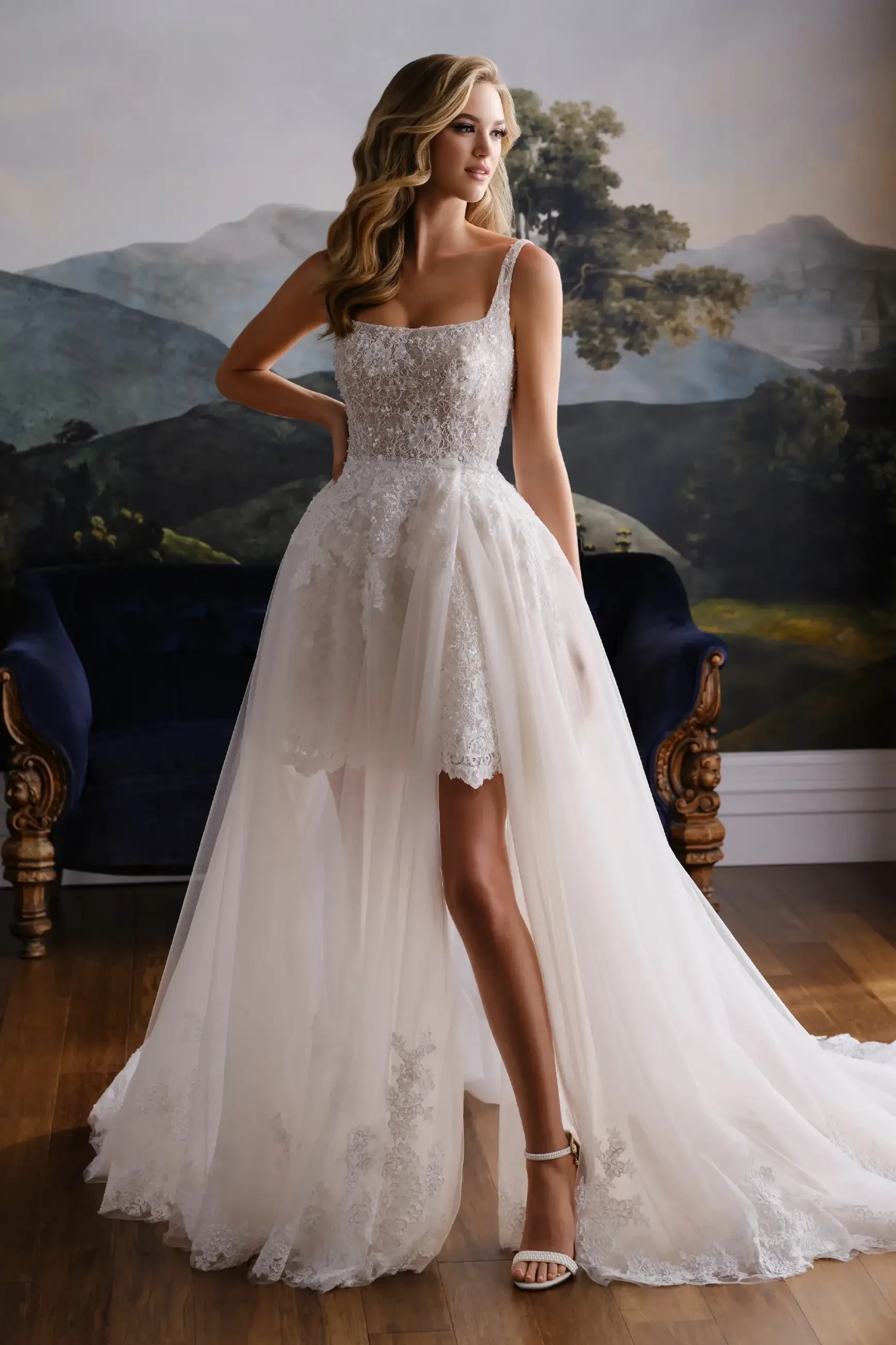 Model is wearing a lace mini wedding dress with a square neckline and a detachable overskirt