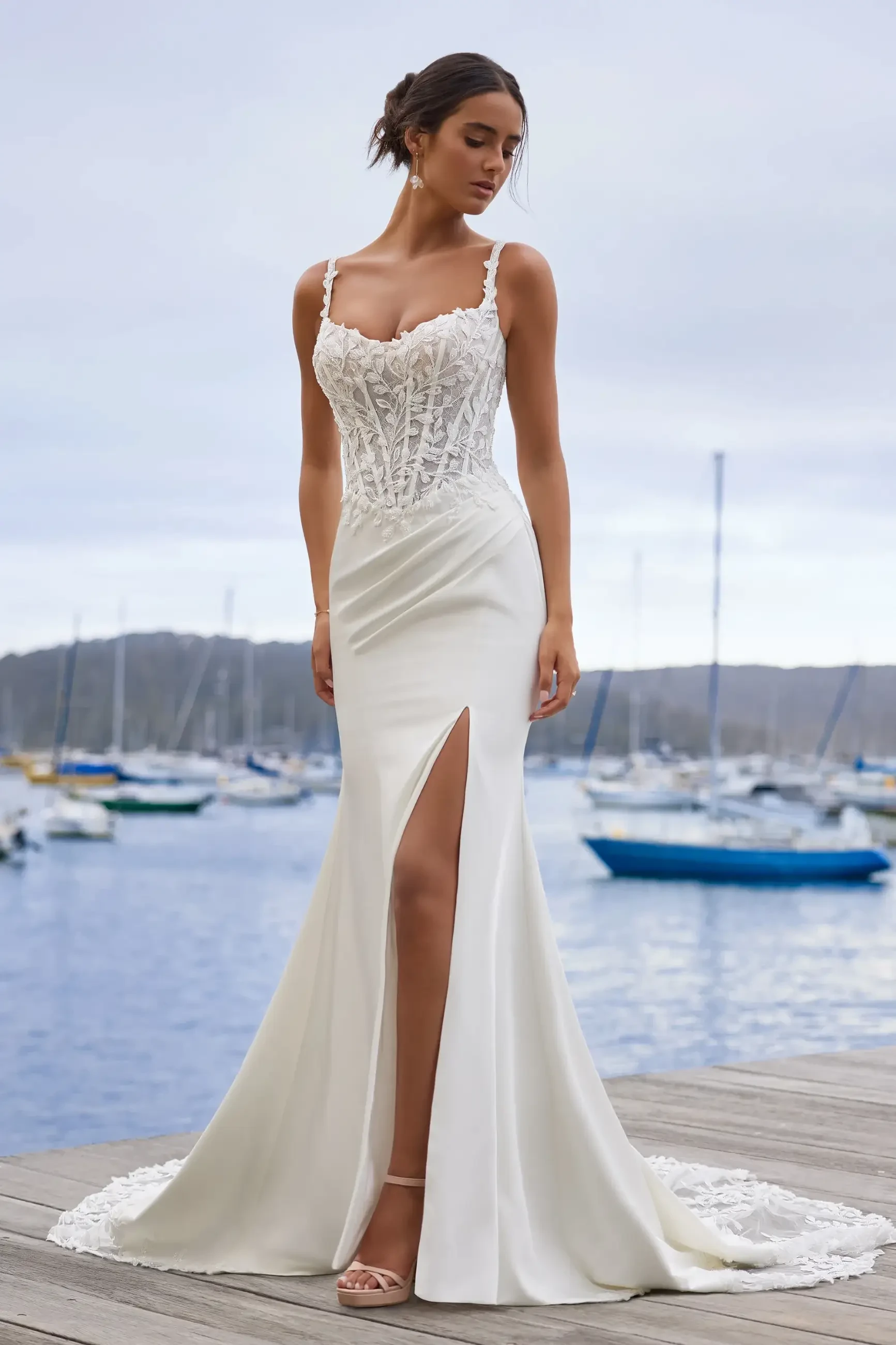 Model is wearing a sleek fit-and-flare gown featuring a semi-sheer corset bodice, high slit, and laser-cut lace details.